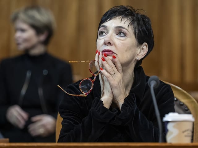 Nachdenkliche Frau im schwarzen Mantel mit Brille in der Hand.