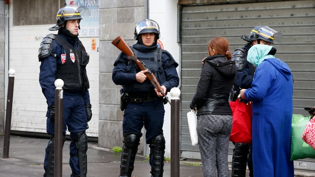 Bewaffnete Polizisten kontrollieren zwei Passantinnen. 