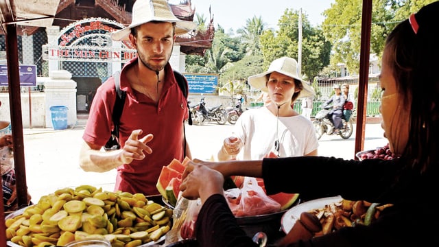 Ein junges Touristenpaar kauft an einem asiatischen Obststand ein. 