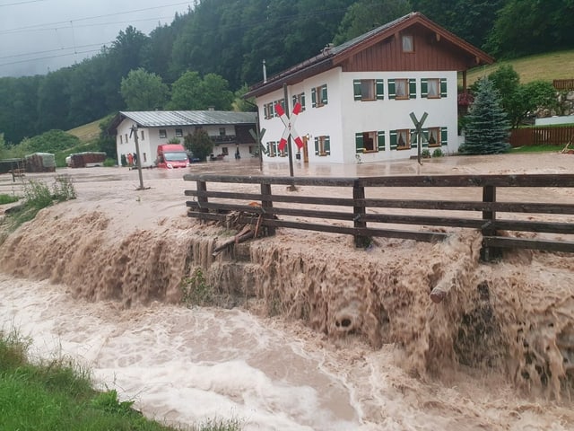 Wasser fliesst über einen Platz vor einem Haus.