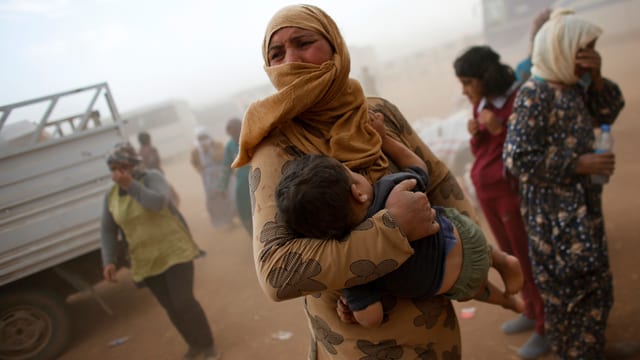 Eine Frau mit einem Baby in der Hand wartet an der syrischen Grenze