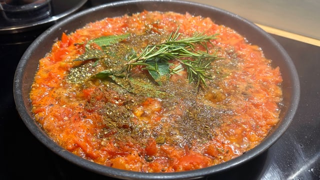 Eine Pfanne mit Tomaten und anderem Gemüse, auf dem Tannennadeln liegen..