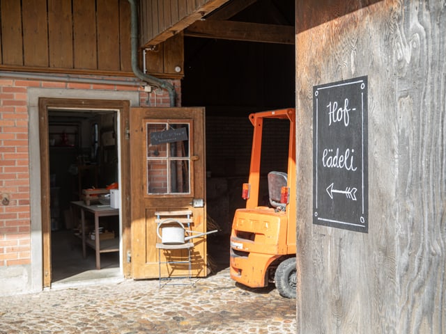 Offene Holztür mit Schild 'Hoflädeli', orange Gabelstapler im Innenhof.