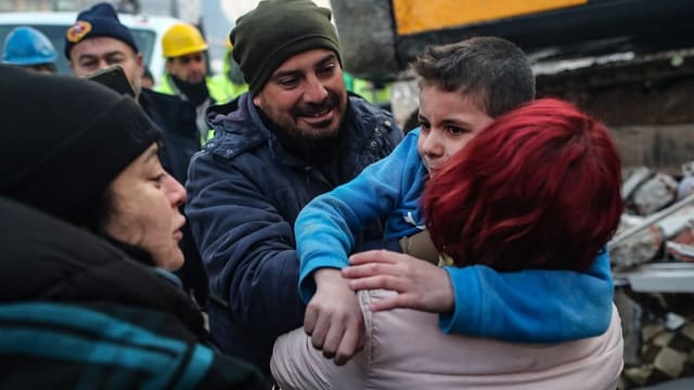 Lachende Helfer übergeben Yigit seiner Mutter