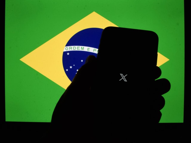 Ein Handy mit dem X-Logo im Vordergrund, dahinter eine Brasilienflagge