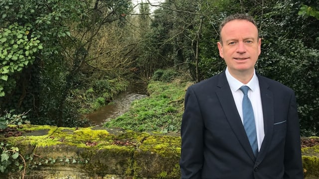  Stephen Kelly im Anzug und mit Krawatte. Reine Haut, leichtes Lächeln. Hinten viel Wald.