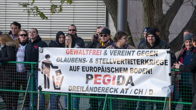 Pegidademonstration: Ein Transparent ist an einem zaun befestigt und dahinter steht eine Gruppe von Menschen.