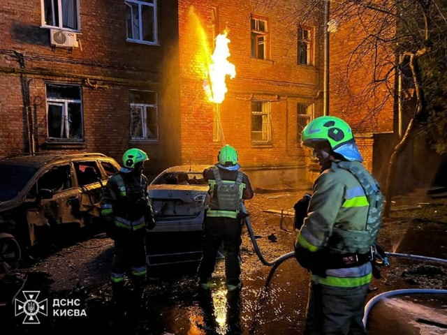 Feuerwehrleute löschen ein brennendes Gebäude und Autos in der Nacht.