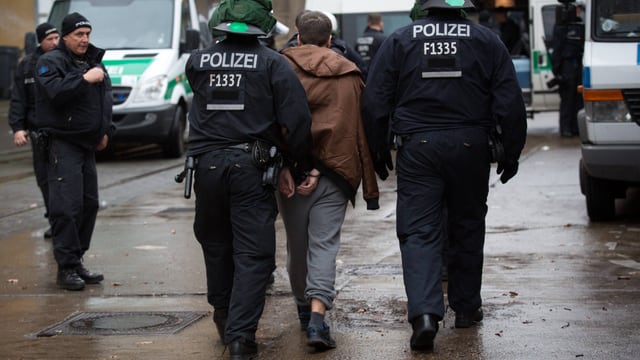 Polizisten führen Mann in Handschellen ab