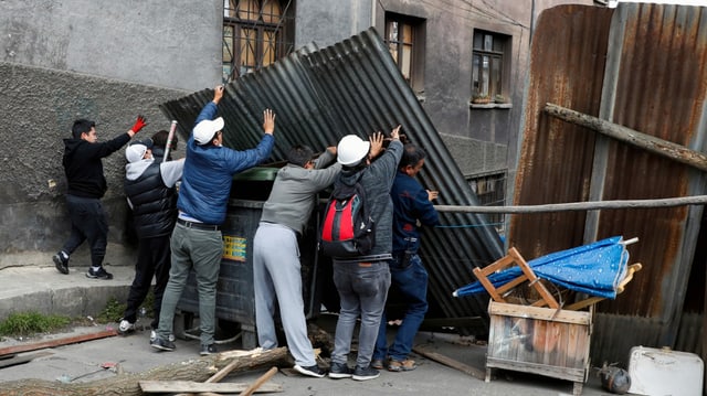 Mehrere Personen erstellen eine Wand aus Wellblech in einer Strasse.