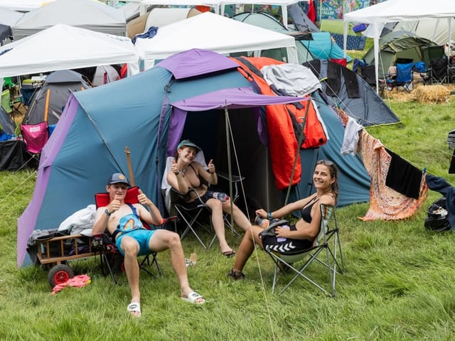 3 Besucher:innen vor ihrem Zelt