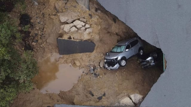 Ein Auto liegt unter einer Strasse in einem Loch, das durchgebrochen ist. 