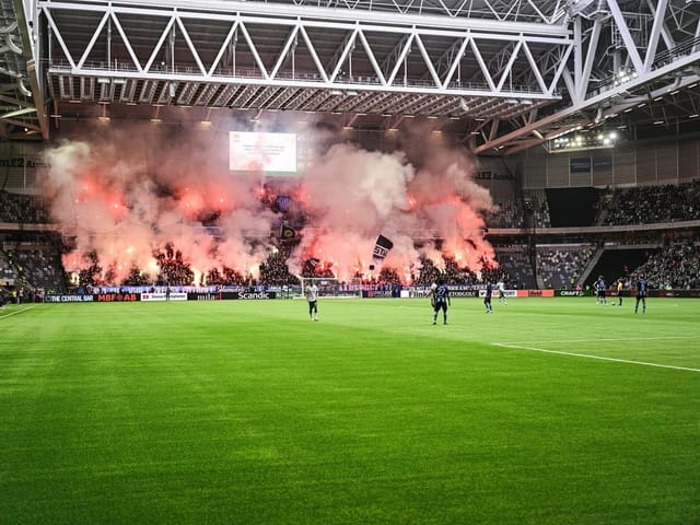 Stadion mit Fussballspiel und Rauch von Fackeln.