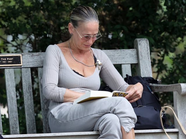 Frau sitzt auf einer Parkbank und liest ein Buch.