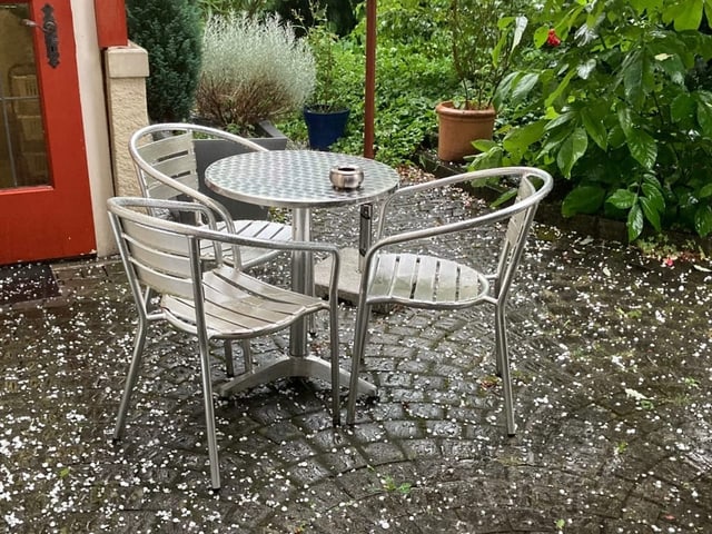 Hagel auf Terrassentisch und Metallstühlen im Garten.