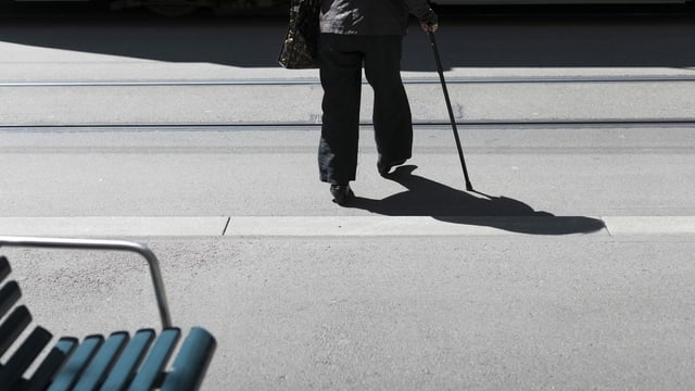 Ältere Frau mit Gehstock überquert Strasse