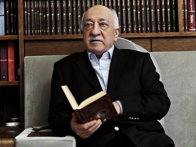 Gülen vor Bücherregal.