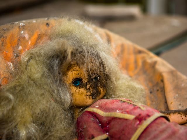 Kleine Puppe mit verfaultem Gesicht, blondem Haar und strahlend blauem Glasauge.