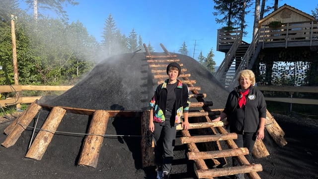 Rebecca Clopath (links) und Köhlerin Doris Wicki (rechts) stehen vor einem der schwarzen Kohlehaufen.