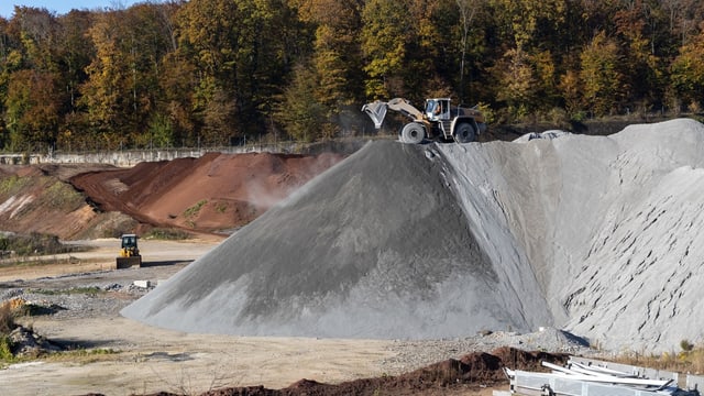 grosse Hügel an sandigem Material, darauf Bagger. Dahinter Wald zu sehen