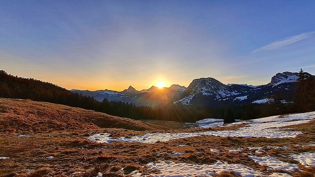 Wiese mit Schneeflecken auf der Sattelegg im Licht der aufgehenden Sonne.