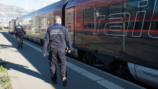 Zwei Grenzwächter stehen vor einem Zug.