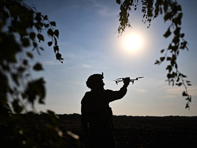 Silhouette einer Person mit Drohne bei Sonnenuntergang.