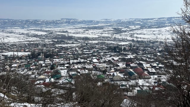 Viele Häuser sind von oben zu sehen. Zwischen ihnen liegt Schnee. Im Hintergrund eine erhöhte Ebene.