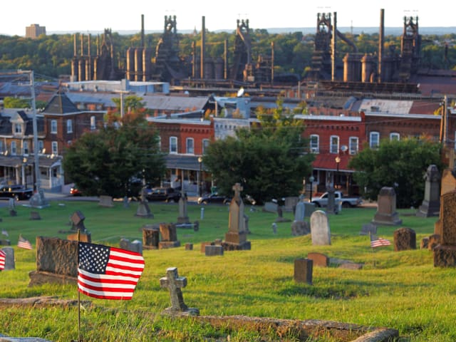 Friedhof mit US-Flaggen, im Hintergrund Industrieanlage.