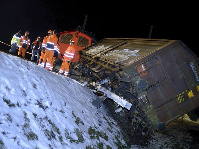 Nachtbild: Waggon halb einen Bahndamm heruntergerutscht.