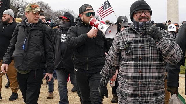 Aufnahme von drei Männern am 6. Januar 2021 in Washington; einer spricht in ein Megafon, ein zweiter lächelt