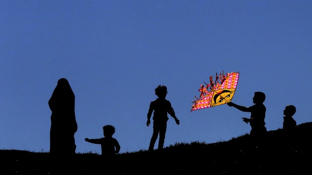 Eine Frau und vier Kinder spielen mit einem Drachen im Wind.