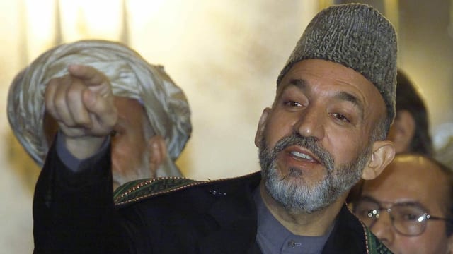 Hamid Karzai points his finger at something or someone.