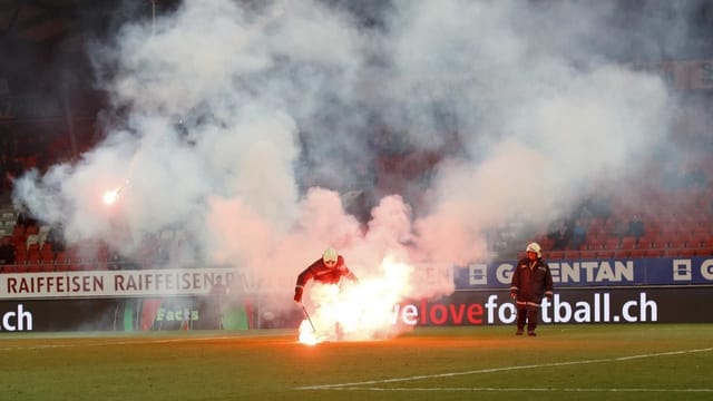 Feuerwehrleute entfernen Leuchtfackeln von Fussballplatz.