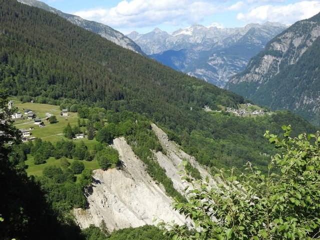 Blick auf bewaldete Berglandschaft mit einigen Häusern im Tal.