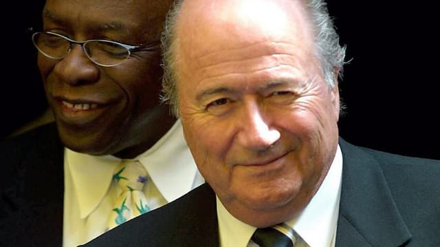 Warner steht hinter Blatter, beide lächelnd und im Anzug.