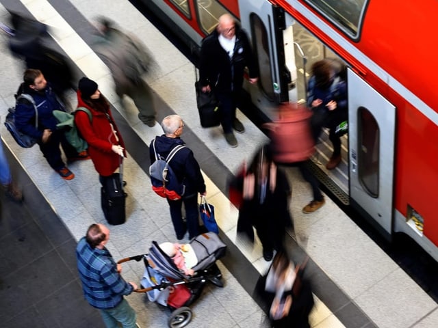 Menschen steigen in einen roten Zug ein.