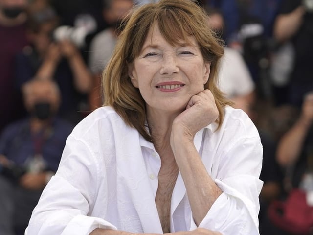 Ein Foto von Jane Birkin. Sie schaut in die Kamera. Im Hintergrund Fotografinnen und Fotografen.