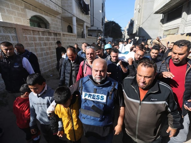 Ein Mann mit "Press"-Veste geht mit Kindern einem Trauerzug voraus