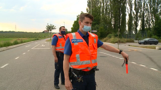 Junger Polizist in Uniform und Leuchtweste bei einer Verkehrskontrolle.