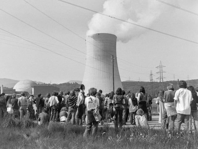 Menschen versammeln sich vor einem dampfenden Kernkraftwerk.