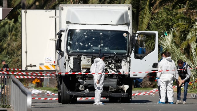 Ein weisser Lastwagen mit Einschusslöchern in der Windschutzscheibe, mehrere Personen in weissen Schutzanzügen stehen darum herum.