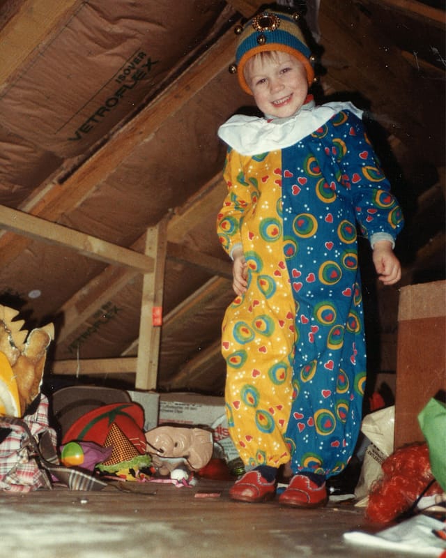 Ein kleiner Bub in einem Clownkostum auf einem Dachboden.