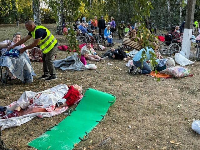 Menschen in Rollstühlen und auf dem Boden sitzen in einem Park.