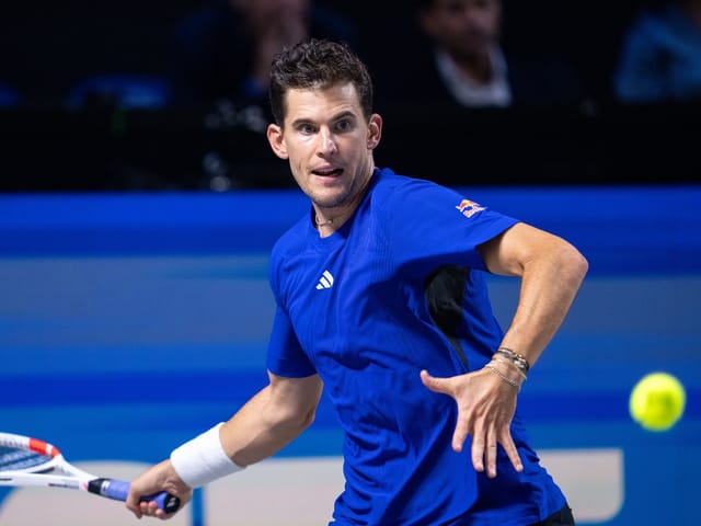 Tennisspieler in blauem Trikot schlägt Ball.