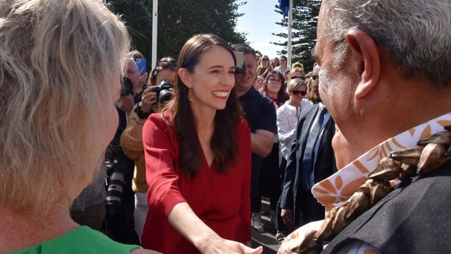 Ardern lächelt Menschen an und grüsst sie. Menschenmenge steht um sie.