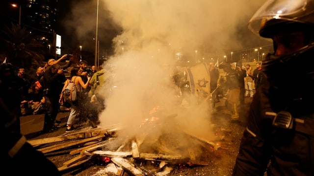 Holzfeuer und Demonstranten mit Blau-Weissen Flaggen