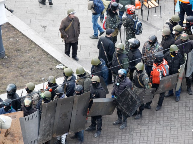 Demonstranten mit Blechschilden stellen sich in einer Reihe auf.