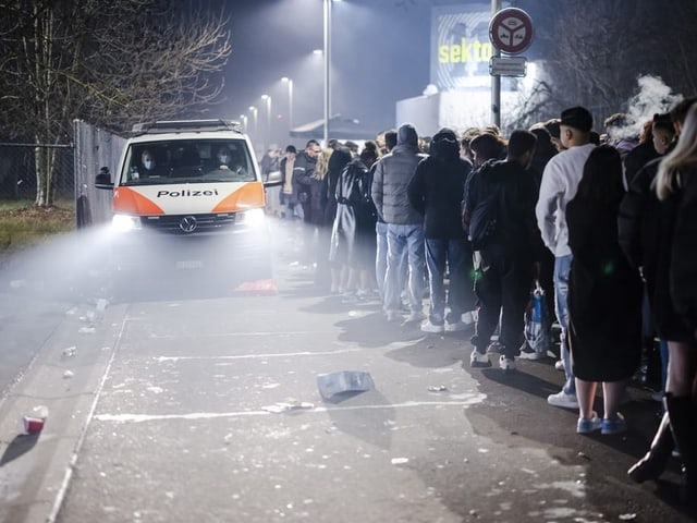 Ein Polizeiauto fährt neben Menschen vorbei