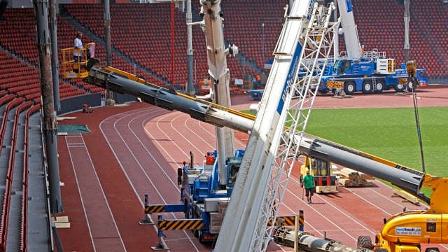 Mehrere Pneukräne stellen im Stadion Letzigrund vor der Tribüne Dachstützen auf.